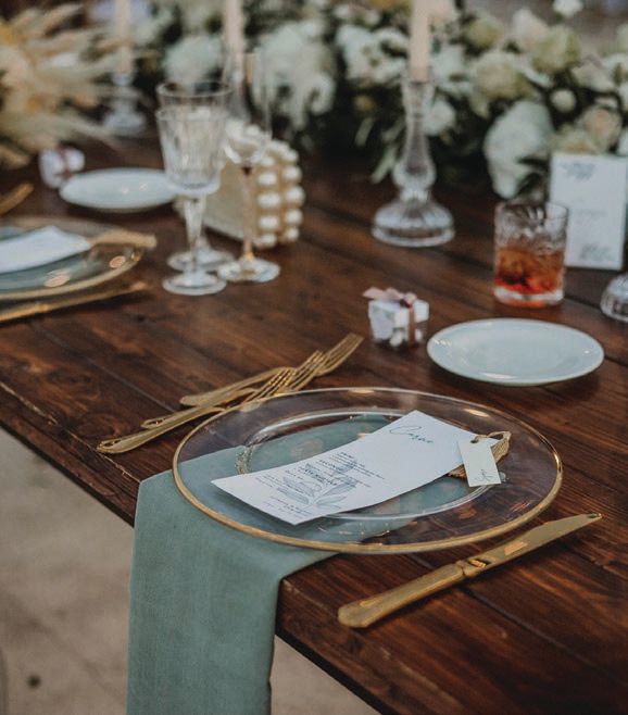 Gold-rimmed glass chargers and flatware accented the natural wood sweetheart table Photographed by Salvatore Cimino