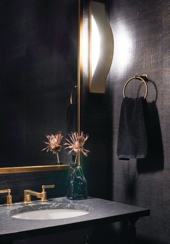 The moody powder room seduces with Studio BK linen metallic gold wallcovering and Visual Comfort Avant linear sconces by Kelly Wearstler Photographed by Anthony Tahlier
